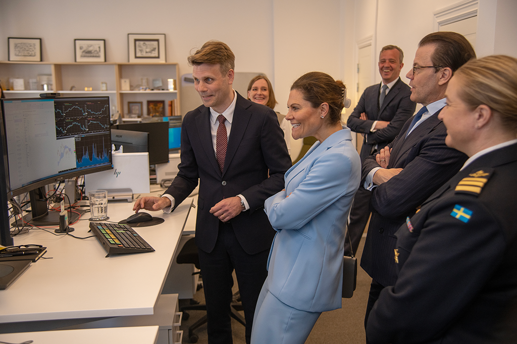 Kronprinsessan och Kronprins Daniel träffar medarbetare från Riksgälden och står framför en datorskärm.